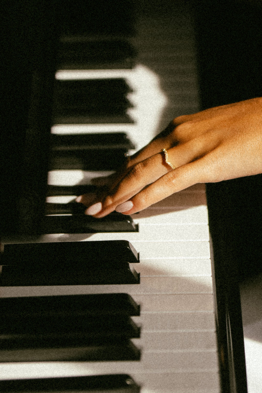 A close-up of a hand resting on piano keys, wearing a thin gold ring on one finger.