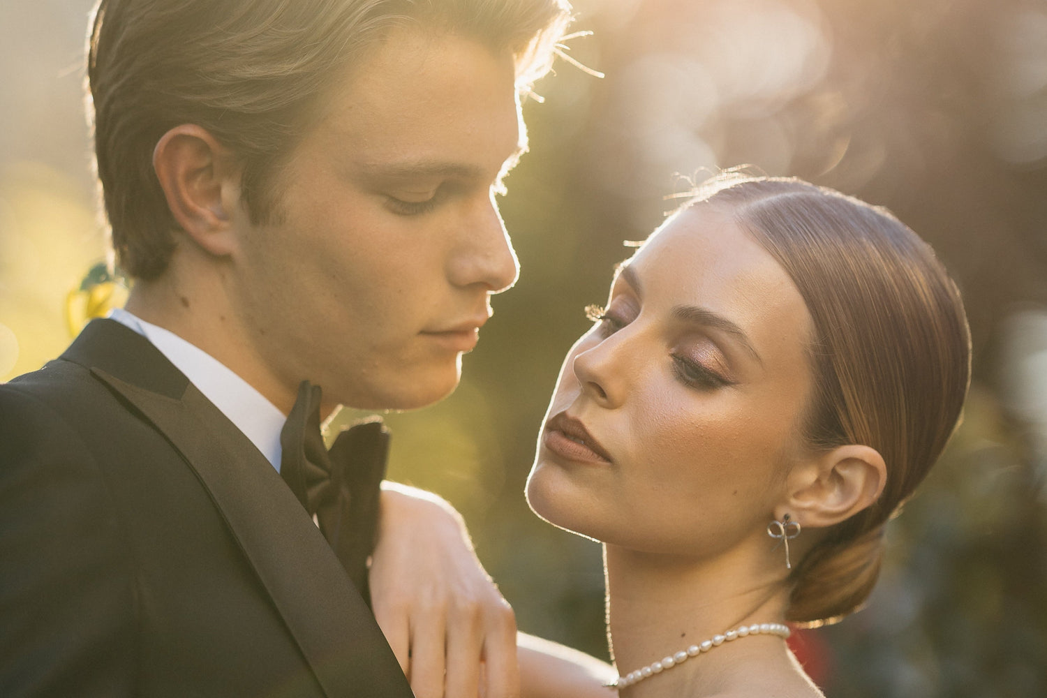 Couple in formal attire embracing outdoors with a warm, blurred background