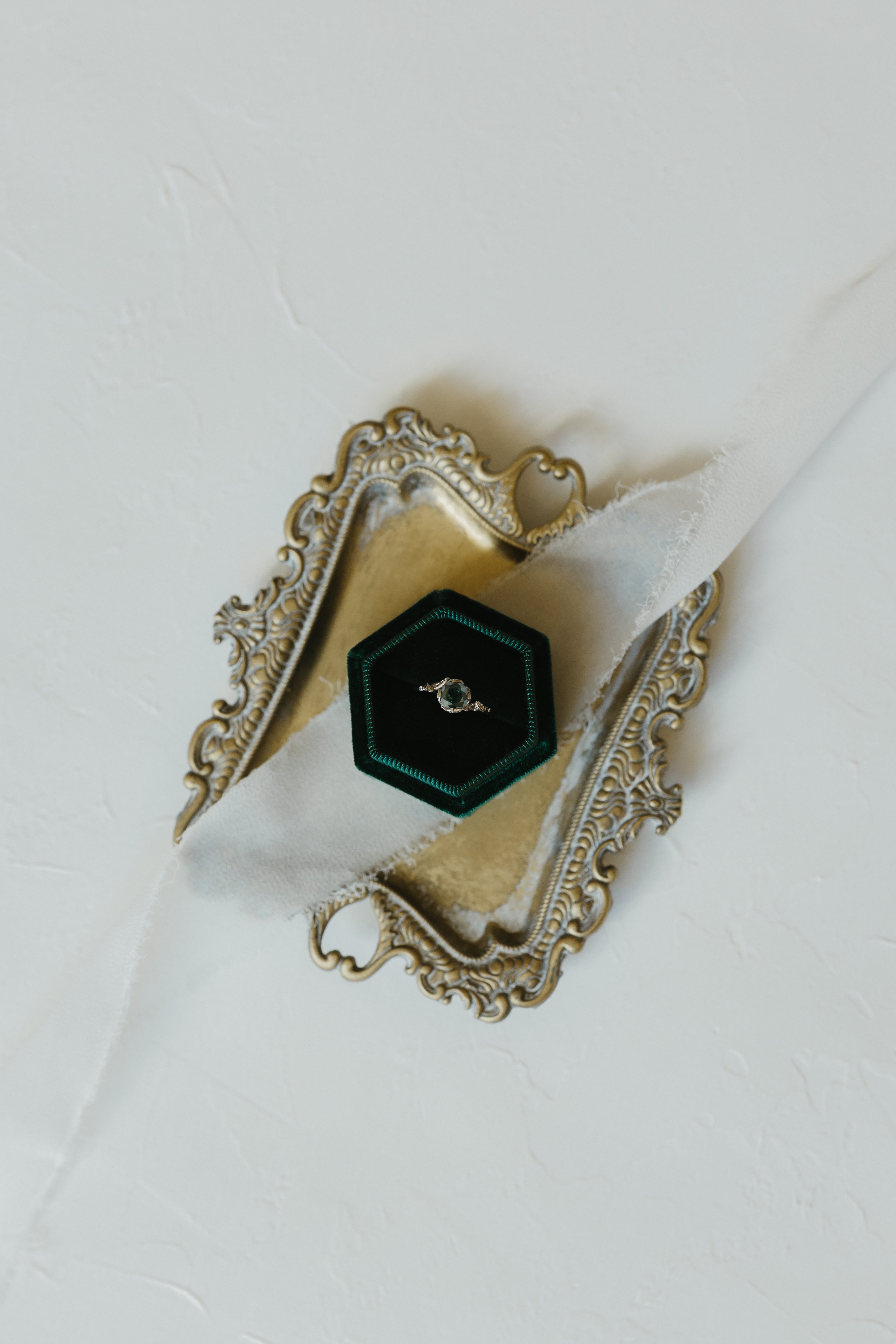 Decorative silver ring box with a green diamond 18k white gold ring made by Tatiana Marques Jewelry on a white background