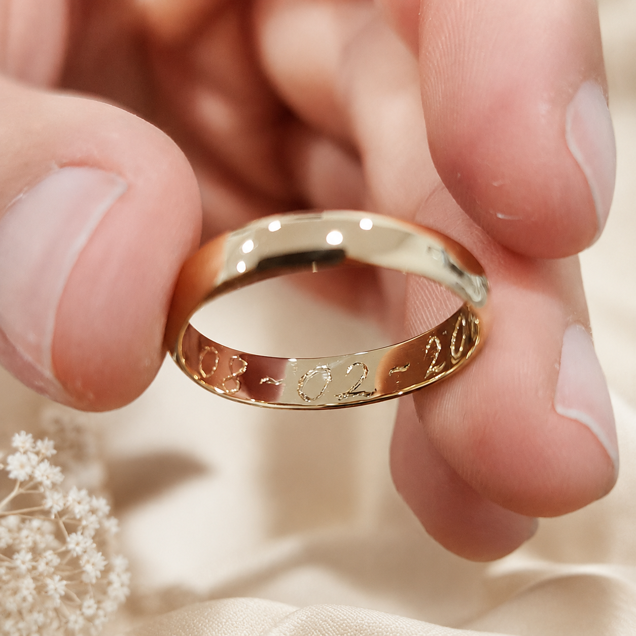 A close-up of a hand holding a polished gold band ring hand engraved with the date, created by Tatiana Marques Jewelry.